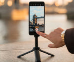 QuadLock Tripod-Selfie Stick håller smartphone stadigt för videoinspelning med Tower Bridge i bakgrunden. Idealisk för vloggare.